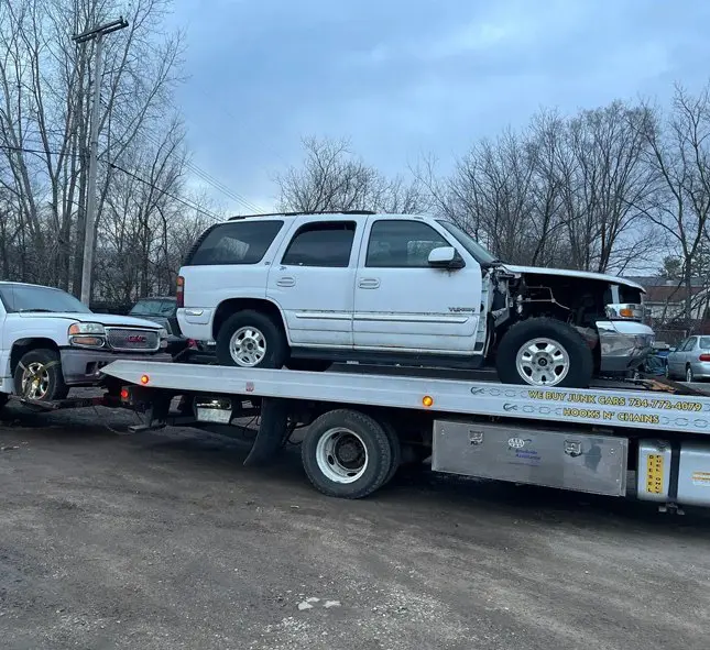 A damaged white SUV being towed on a flatbed truck in a parking lot.
