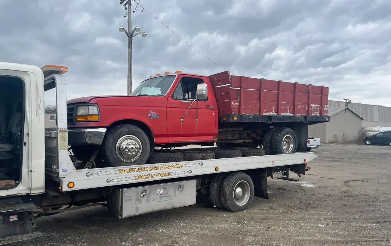 Red flatbed truck loaded on a white tow truck under a cloudy sky.