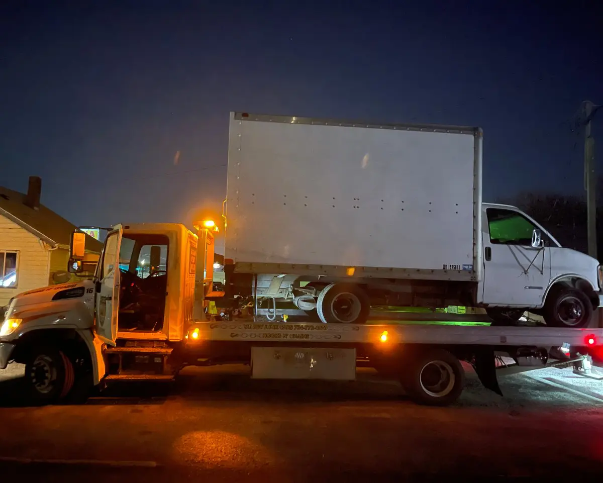 Tow truck carrying a white truck with a graffiti design at night.