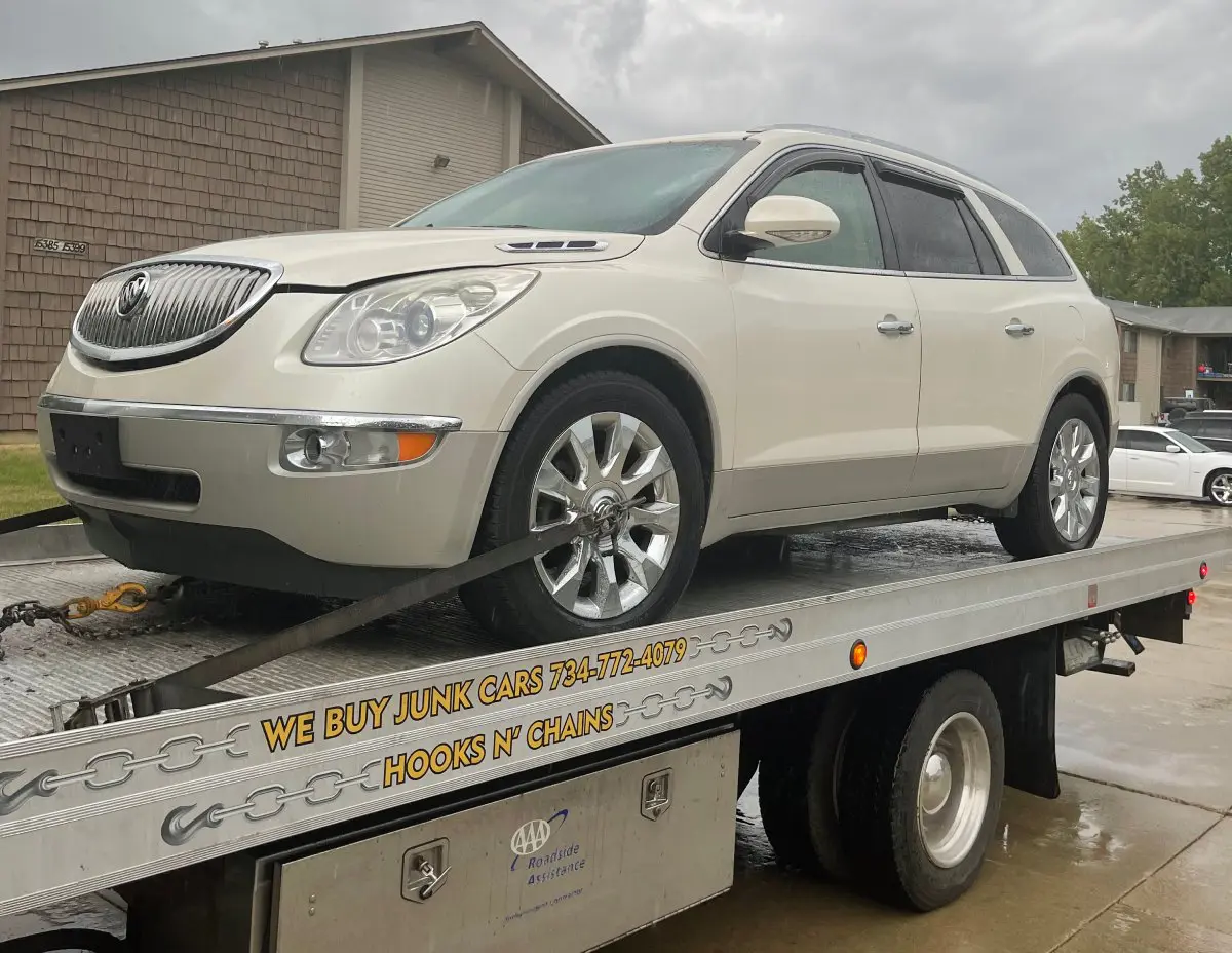 White SUV loaded on a flatbed tow truck under a cloudy sky.