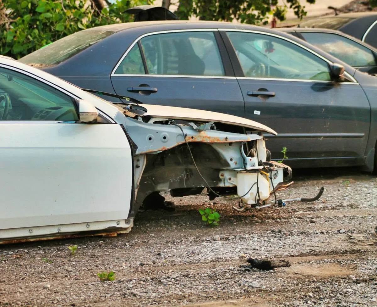 A damaged white car missing its front bumper and wheel.